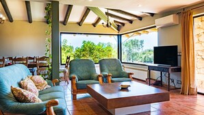 Een woonkamer met een bank, twee fauteuils, een salontafel, een televisie en uitzicht op groen.