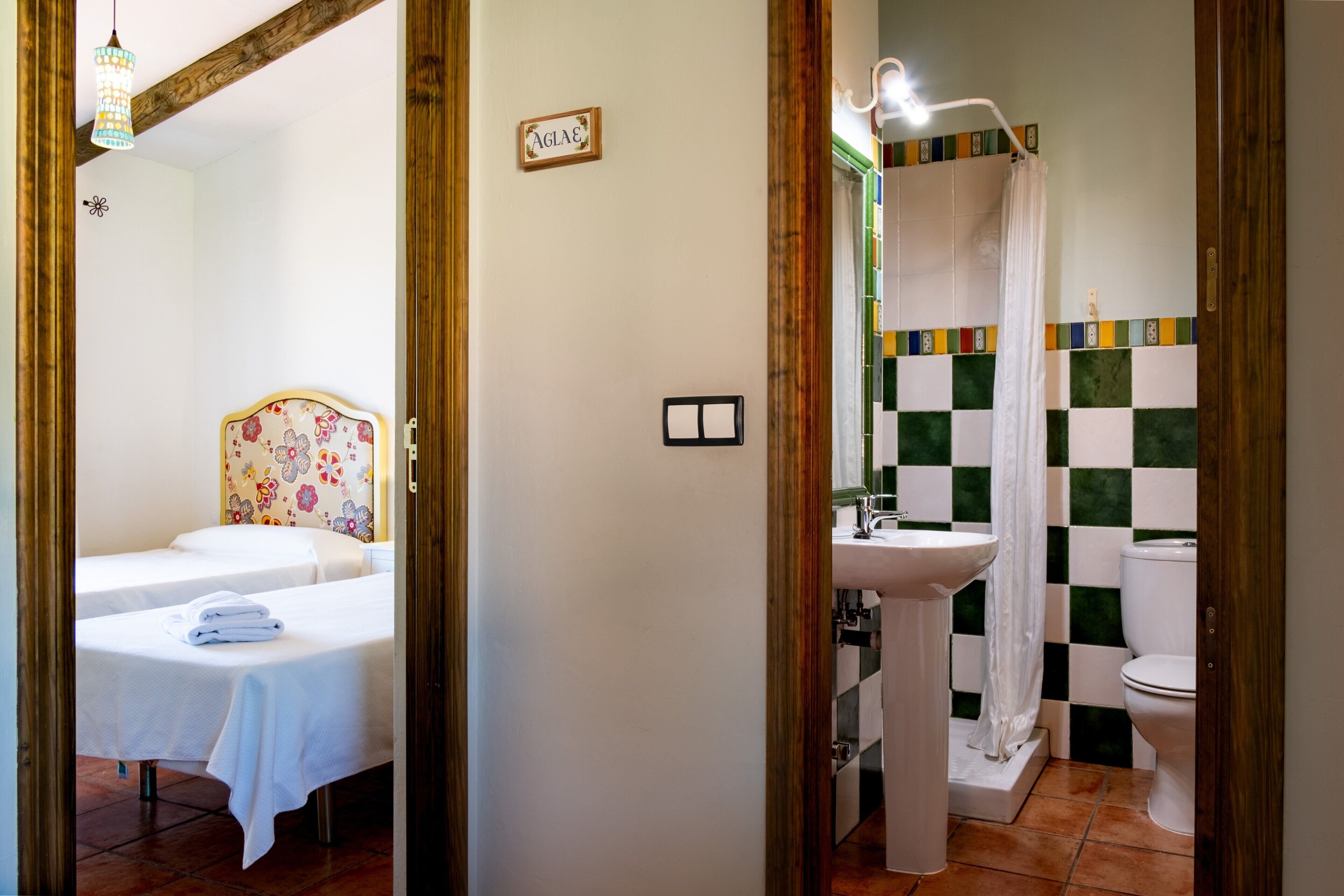 A room with a bed, a bedside table with a lamp, and a bathroom with a sink and toilet.
