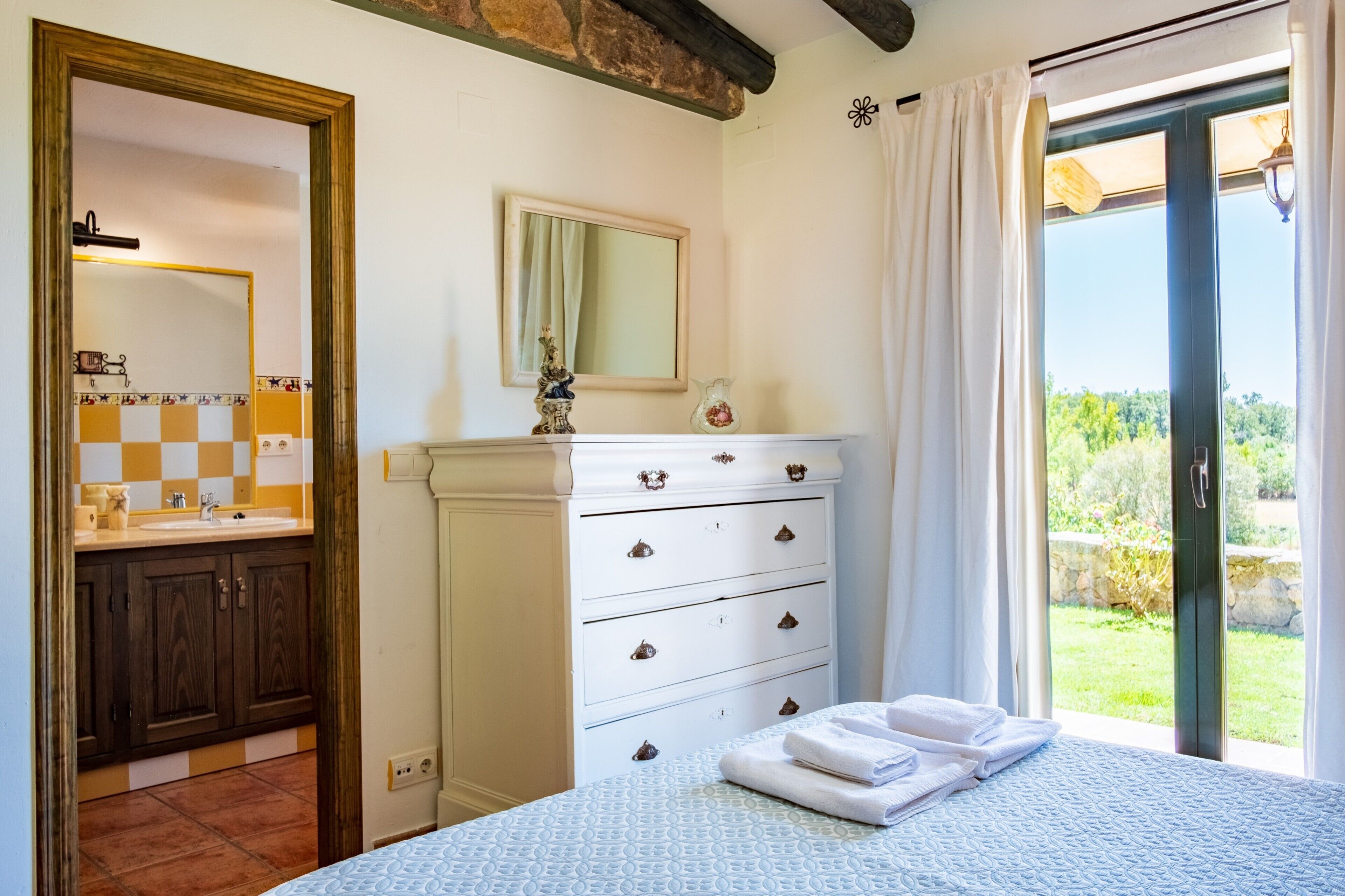 Une chambre à coucher avec un lit, une commode, un miroir et une vue sur l’extérieur.