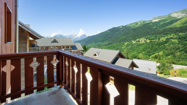 Ein Balkon mit Blick auf eine gebirgige Landschaft, Holzhäuser und einen klaren Himmel.
