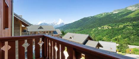 Ein Balkon mit Blick auf eine gebirgige Landschaft, Holzhäuser und einen klaren Himmel.
