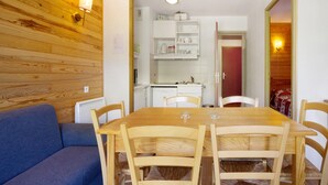 Ein Essbereich mit Holztisch und -stühlen, einem blauen Sofa und einer Küchenzeile mit weißen Schränken und einer roten Tür.