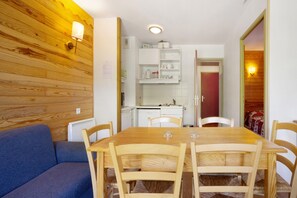 A dining area with a wooden table and chairs, a blue sofa, and a kitchen area with white cabinets and a red door.