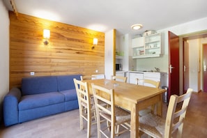 A dining area with a wooden table and chairs, a blue sofa, and a kitchen in the background.
