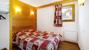 Ein Schlafzimmer mit einem hölzernen Kopfende, einer gesteppten Bettdecke, einem Fenster mit Vorhängen und einer Wandleuchte.