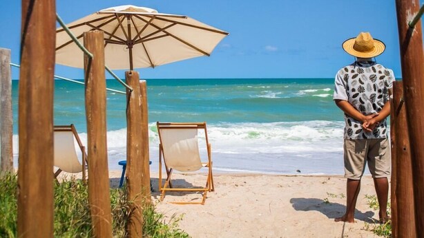 A beach scene with a wooden fence, a beach umbrella, and two beach chairs. - Viva Barra Hotel Pousada (Barra de São Miguel)