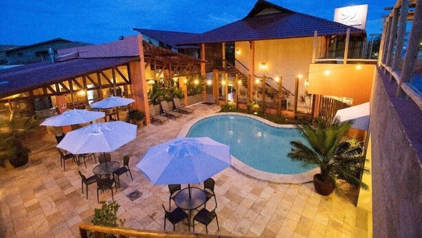 An outdoor pool area with lounge chairs and umbrellas, surrounded by a building with a covered patio and a staircase leading to an upper level. - Viva Barra Hotel Pousada (Barra de São Miguel)