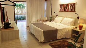 Quarto de hotel com cama, mesa de cabeceira, abajur e vista para o exterior pela janela.