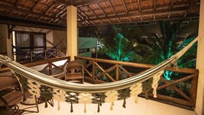A hammock chair set up on a balcony with a view of palm trees and a thatched roof structure. - Viva Barra Hotel Pousada (Barra de São Miguel)