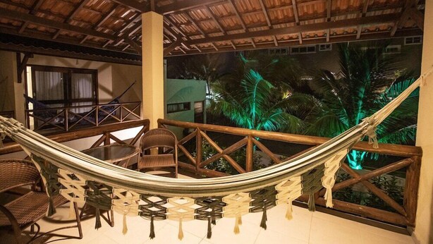 A hammock chair set up on a balcony with a view of palm trees and a thatched roof structure.