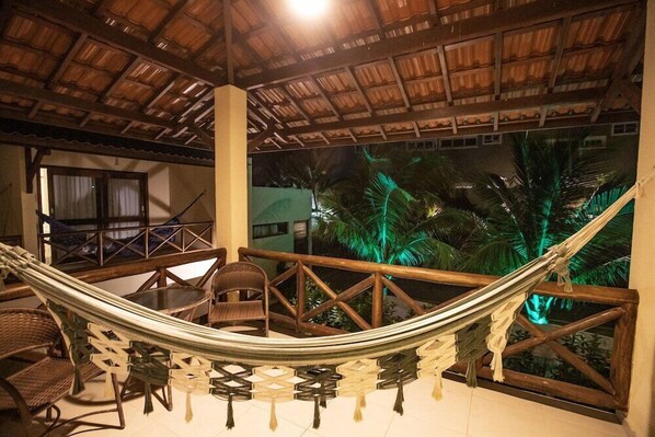 A hammock chair set up on a balcony with a view of palm trees and a thatched roof structure. - Viva Barra Hotel Pousada (Barra de São Miguel)