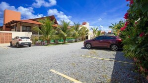 A parking area with two cars, a building with a red roof, and palm trees.