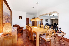 A dining area with a wooden table and chairs, a chandelier, and a stone fireplace.
