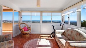 A sunlit room with a view, a wicker chair, a sofa, and an exercise bike. - Country House 'Quinta Da Violeta' with Sea View, Wi-Fi and Air Conditioning (Loulé)