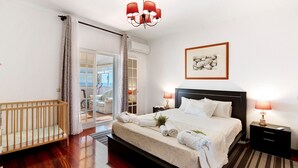 A hotel room with a bed, bedside lamps, a crib, a door leading to a balcony, and a framed picture on the wall. - Country House 'Quinta Da Violeta' with Sea View, Wi-Fi and Air Conditioning (Loulé)