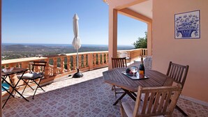 A terrace with a table set for two, a chair, and an umbrella. - Country House 'Quinta Da Violeta' with Sea View, Wi-Fi and Air Conditioning (Loulé)