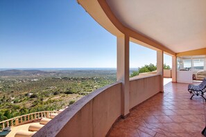 A balcony with a view of a hilly landscape, a tiled floor, and a bench.