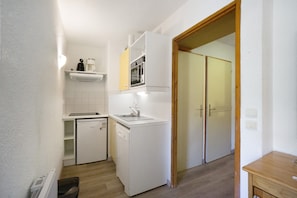 A compact kitchen with a dishwasher, a sink, and a microwave. There is a wooden door leading to another room.