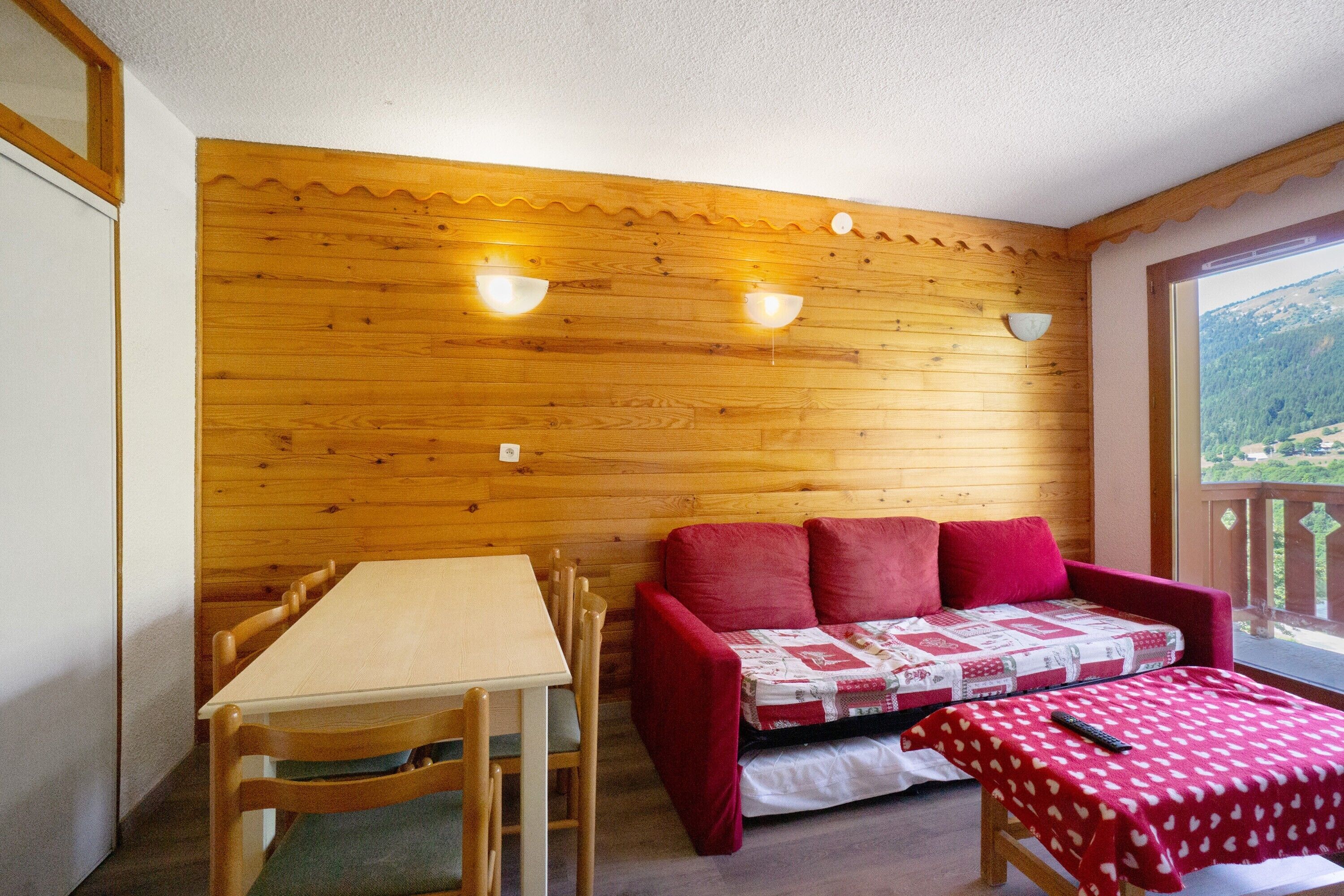 Ett rum med träpanel på väggarna, ett bord, stolar, en röd soffa och utsikt över omgivningen.
