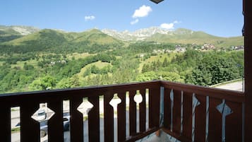 A balcony with a view of a mountainous landscape, a parking area, and a building with traditional architecture.
