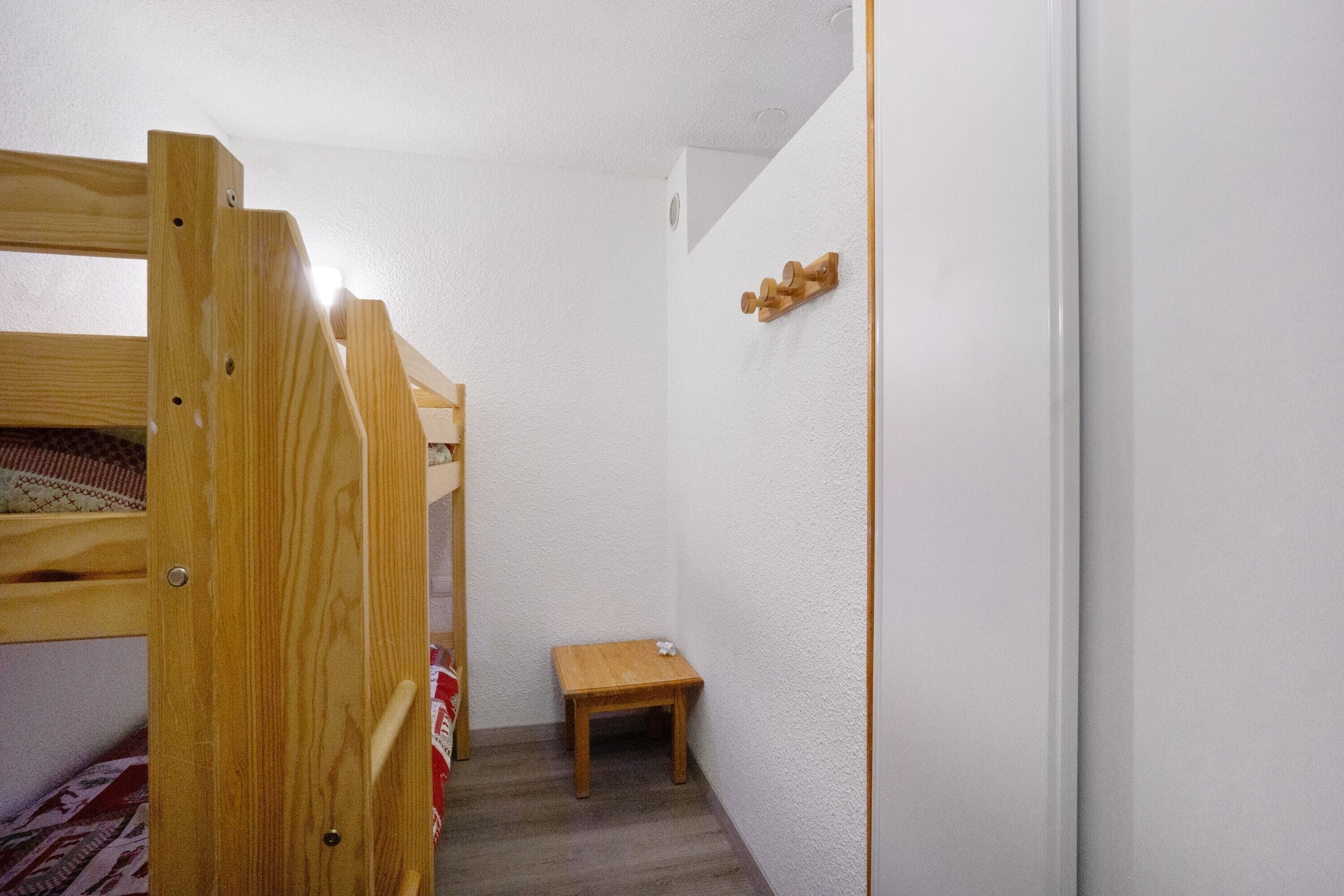 Una habitación con una cama litera, una mesita de madera y una pared blanca con un estante de madera.