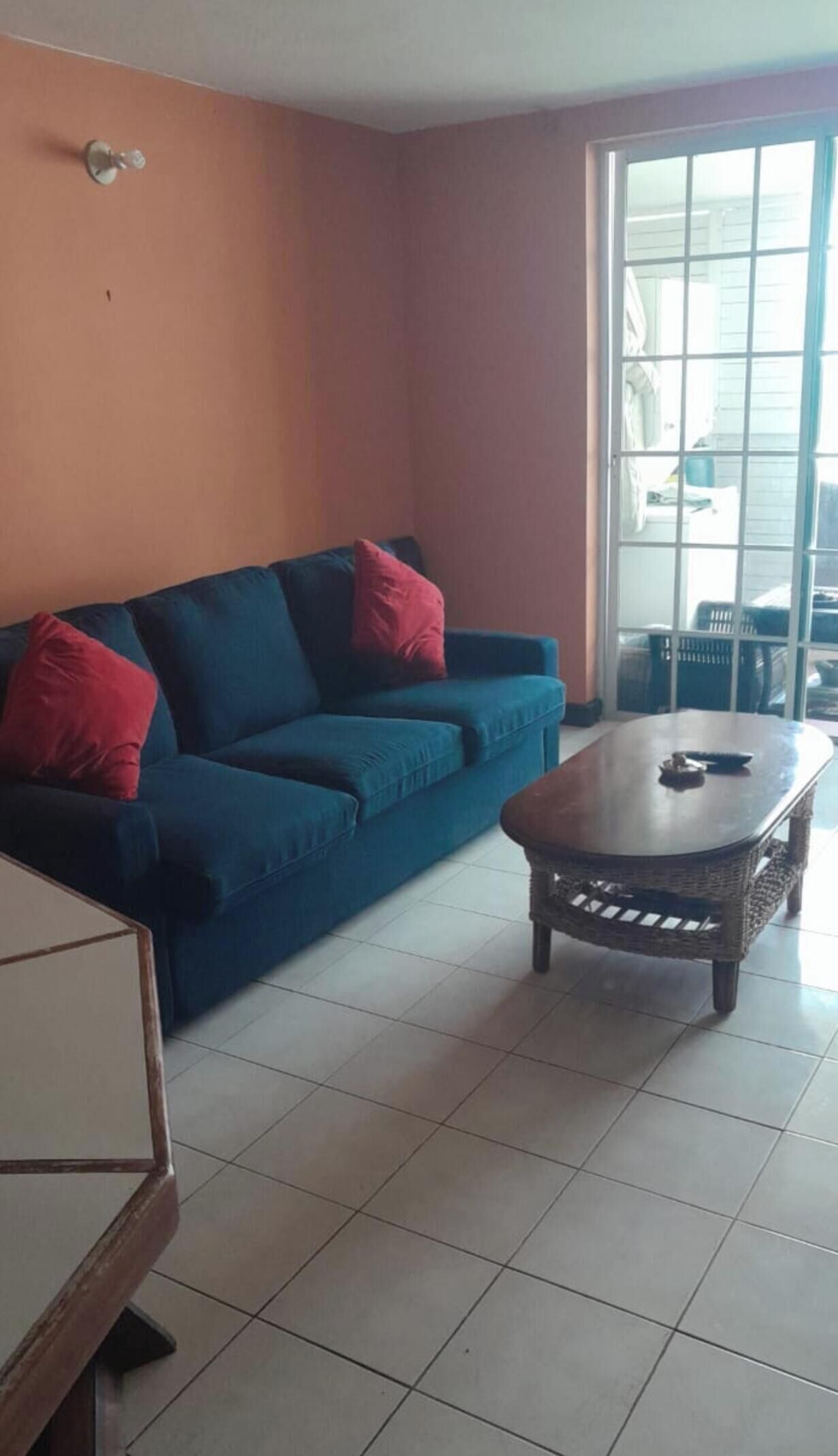 Ein Wohnzimmer mit einem blauen Sofa, roten Kissen, einem Holztisch und einer Glastür zum Balkon.