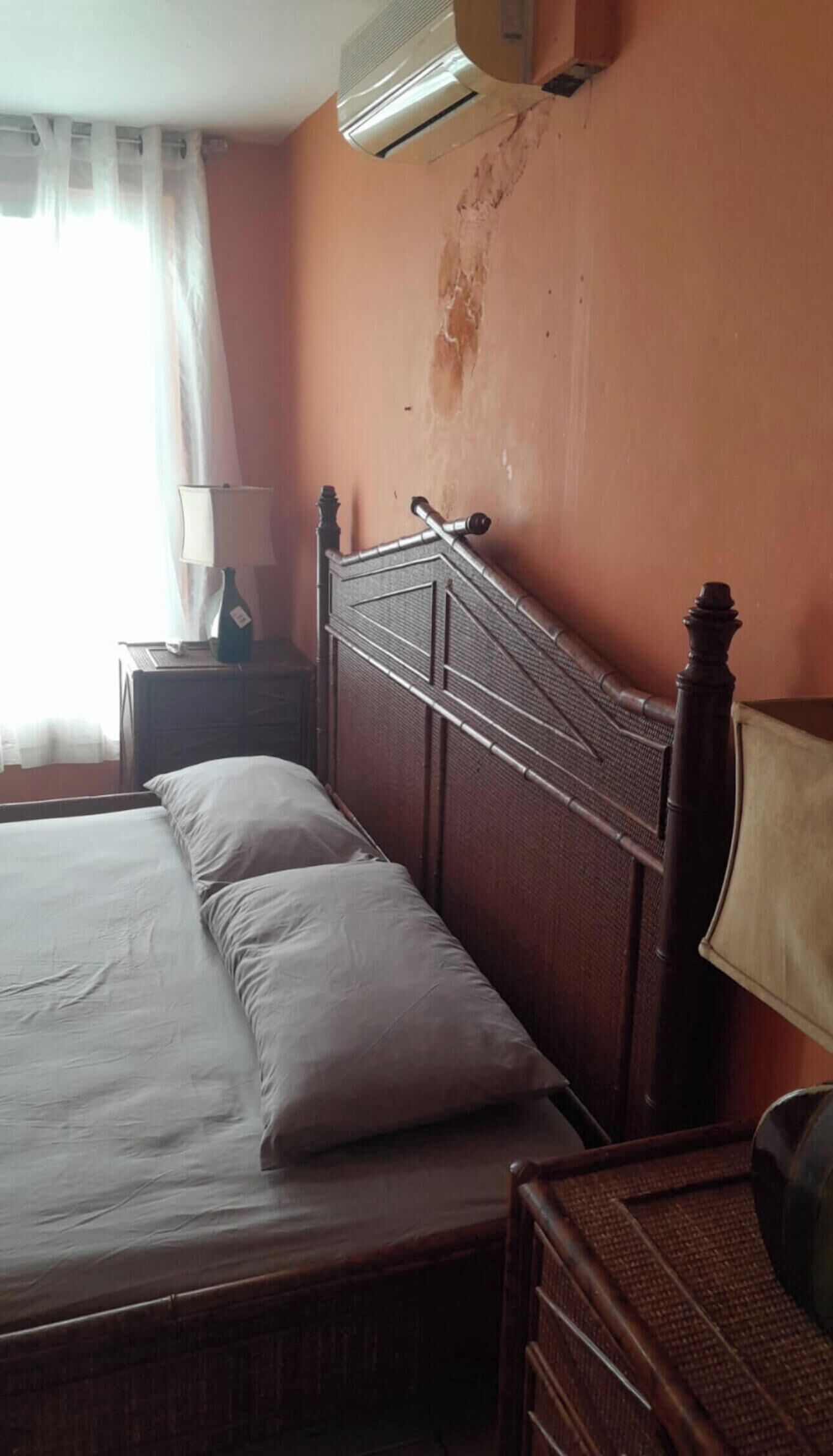 Un dormitorio con cama, mesita de noche, lámpara y aire acondicionado.