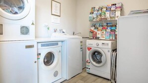 Une buanderie équipée de deux machines à laver, d’un sèche-linge et d’une étagère contenant divers produits de nettoyage.