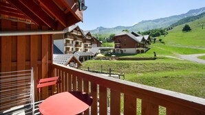 Ein Holzbalkon mit einem roten Tisch und Stühlen, der einen Blick auf ein Hotel mit mehreren Gebäuden und einer Bergkulisse bietet.