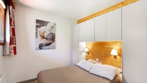Ein Schlafzimmer mit einem hölzernen Kopfteil, einem Bett mit weißen Bettwäsche und einem an der Wand hängenden Bild von einem Eisbären, sowie einem Fenster mit Vorhängen.