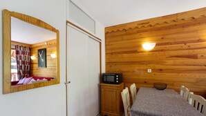 Ein gemütlicher Raum mit Holzwand, einem Esstisch mit Stühlen, einer Mikrowelle und einem Spiegel.