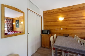 Une pièce de taille modeste avec un mur en bois, une table à manger avec des chaises, un four à micro-ondes et un miroir.
