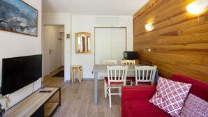 Ein Wohnzimmer mit Fernseher, Holzvertäfelung, einem Essbereich mit Stühlen und einem roten Sofa.
