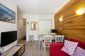 Un salon équipé d’un téléviseur, avec un lambris en bois, un coin repas avec des chaises et un canapé rouge.