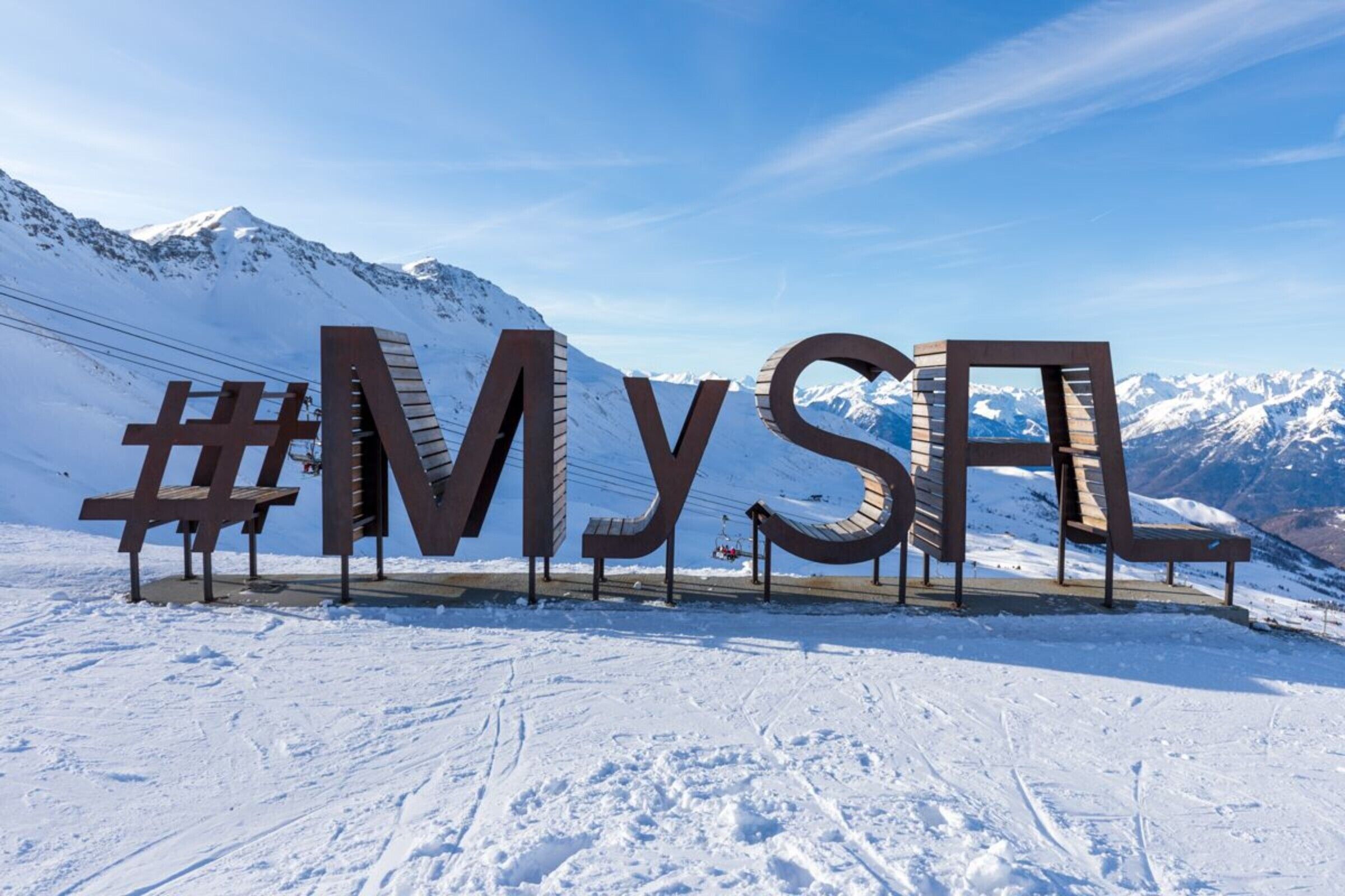 Een groot buitenbord met de letters 'MYS' in een bergachtig, besneeuwd landschap.
