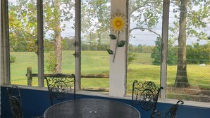 Una habitación con una mesa redonda y cuatro sillas, ventanas amplias con vistas a un campo cubierto de hierba y árboles, y una decoración de girasol en la pared.