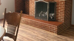 Una habitación con chimenea de ladrillo, piso de madera y ventilador de techo.