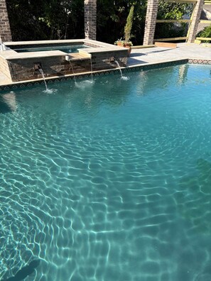 A clear swimming pool with a stone border and a water feature.