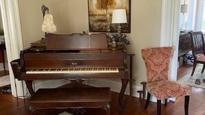 A grand piano in a living room with a floral rug, a chair, and a painting on the wall. - The Stinson Suite, Jenny's Downtown Hideaway Bed and Breakfast-The Stinson Suite (Laurel)