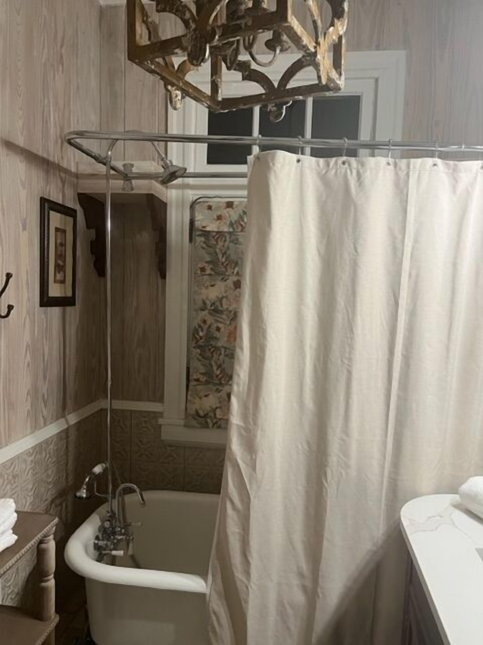 A bathroom with a clawfoot bathtub, a shower with a floral shower curtain, and a wooden vanity with a towel.