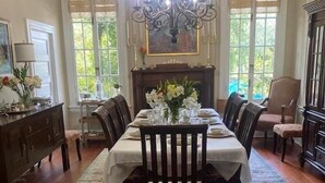 Une salle à manger agrémentée d’un lustre, d’une cheminée et offrant une vue sur la verdure grâce à de grandes fenêtres.