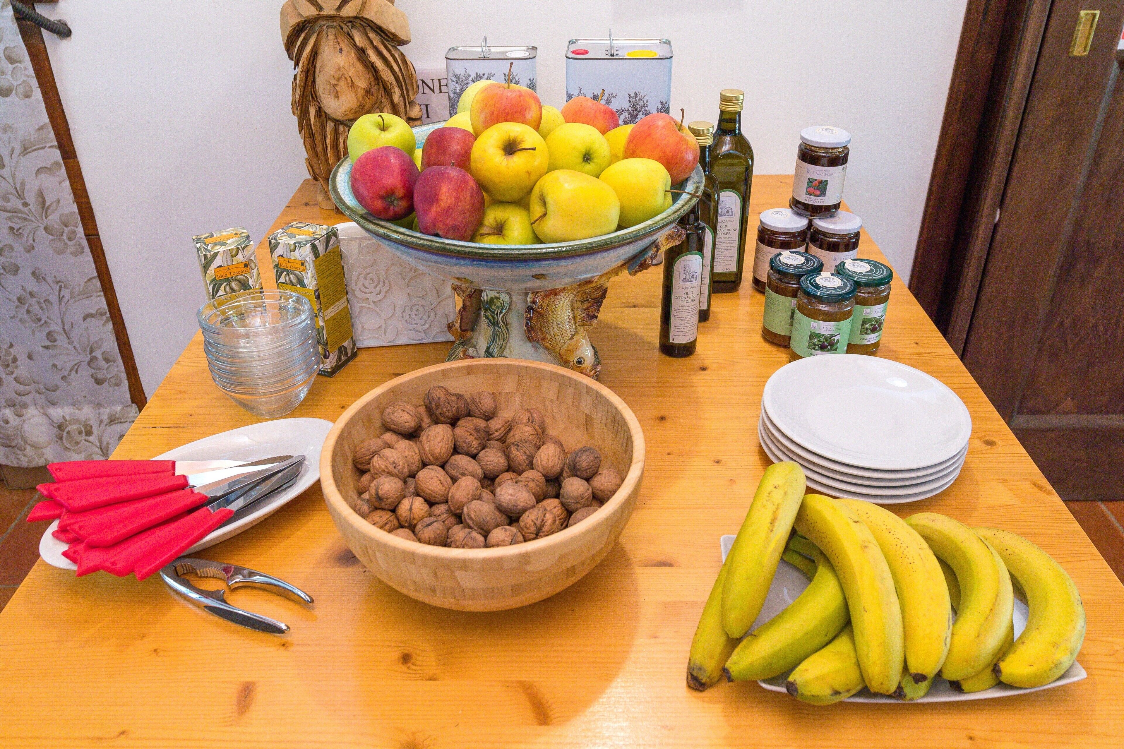 A wooden table with a bowl of nuts, a plate of bananas, and a bowl of apples.