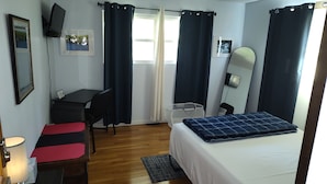 Ein Hotelzimmer mit Bett, Schreibtisch, Stuhl, Fernseher und einem fenster mit Vorhängen.