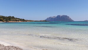 Ein Strand mit klarem türkisblauem Wasser, einem felsigen Vorsprung in der Ferne und einem sandigen Ufer.