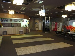 A reception area with a counter, a receptionist, and a wall with framed pictures. - Taisetsuzan Shirogane Kanko Hotel (Biei)