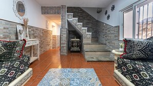 A living room with patterned sofas, a fireplace, a staircase with patterned tiles, and a view through a window.