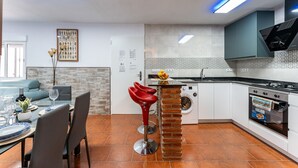 A modern kitchen with a central island, a dining area with a table and chairs, and a living room with a sofa.