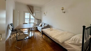 Une pièce de taille modeste comprenant un lit, une table à manger, deux chaises, un canapé et une fenêtre avec des rideaux.