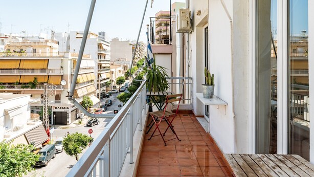 Un balcon donnant sur la rue, une plante en pot et une chaise pliante.