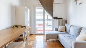 Une pièce avec une table en bois, un canapé gris, une armoire blanche et une porte-fenêtre coulissante donnant sur un balcon extérieur.